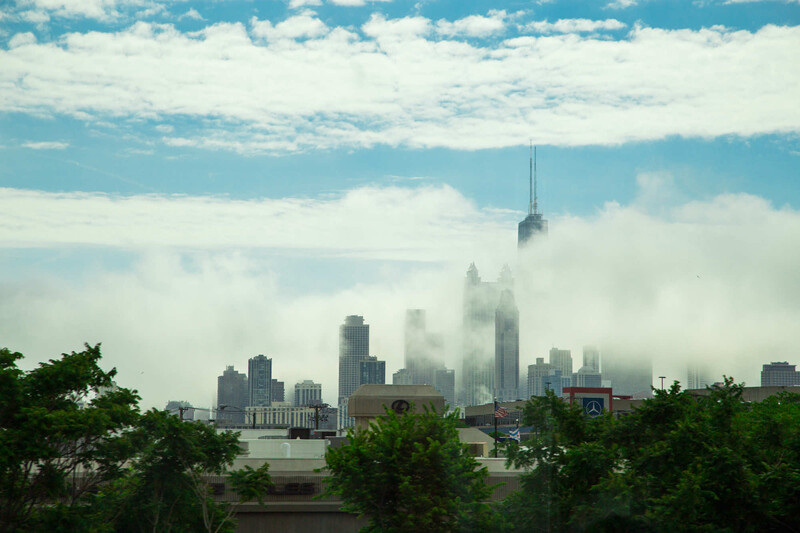 City skyline partially shrouded in thick fog and low clouds under blue sky.