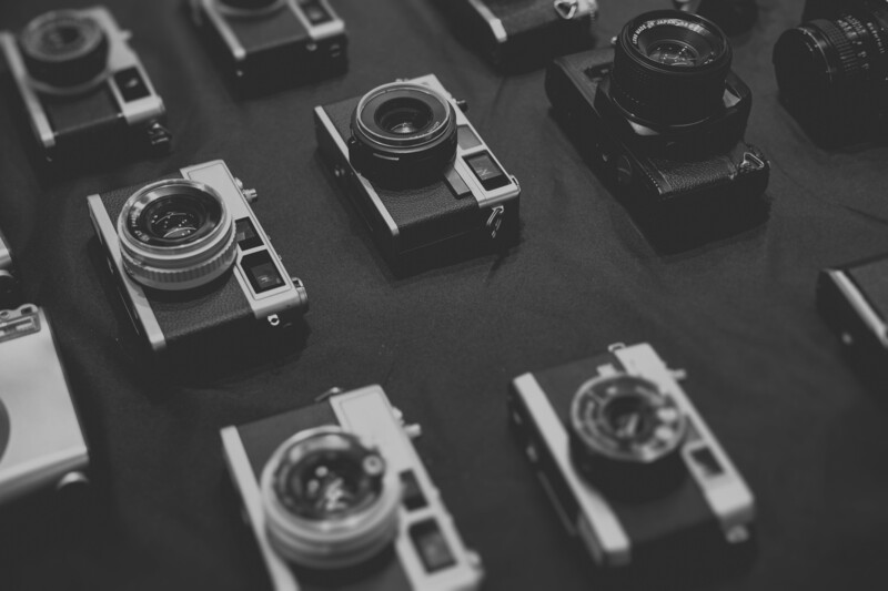 Collection of vintage rangefinder cameras arranged on a dark surface in black and white.
