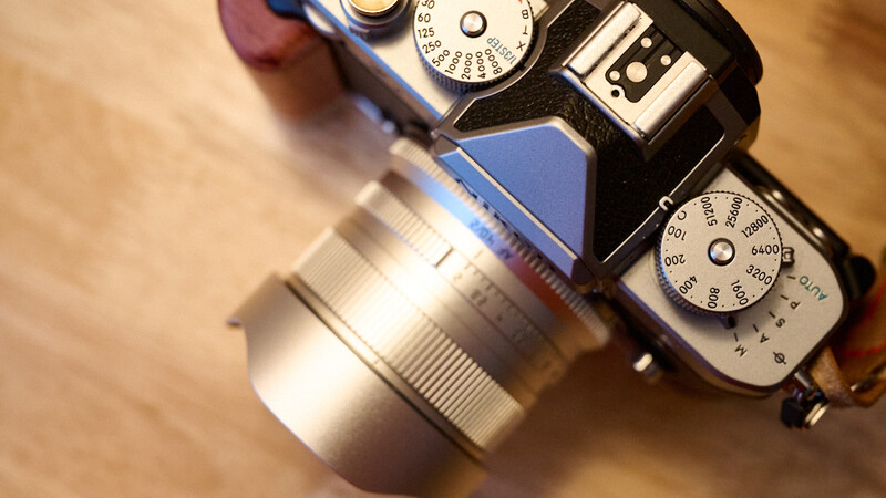 Blue mirrorless camera with silver prime lens mounted, displayed from above on wooden surface.