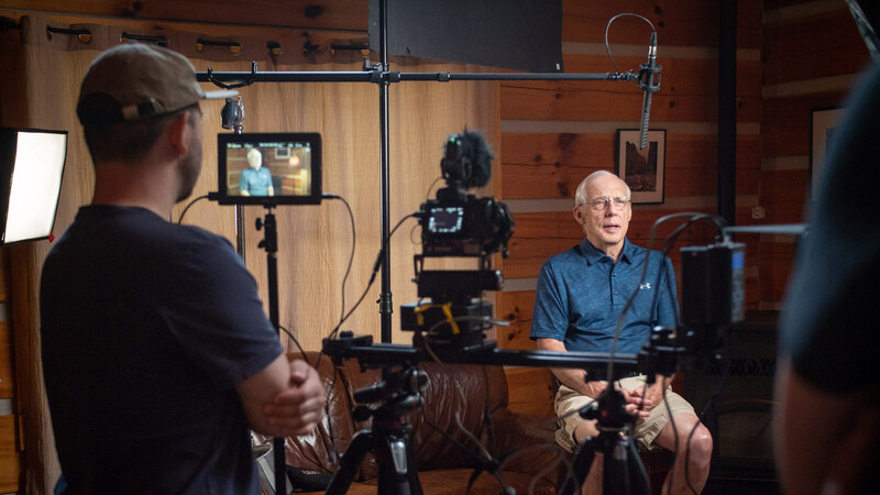 Professional video production setup with subject seated before multiple cameras and lighting rigs in a wooden studio.
