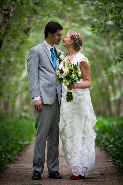 Bride and groom walking together on a tree-lined path, bride holding white bouquet.