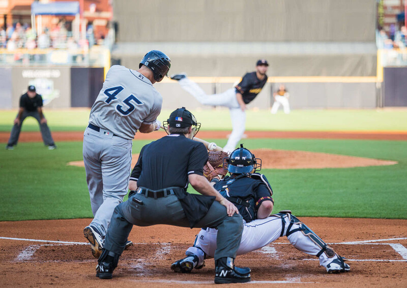 Baseball batter mid-swing during a game with catcher and umpire in frame.