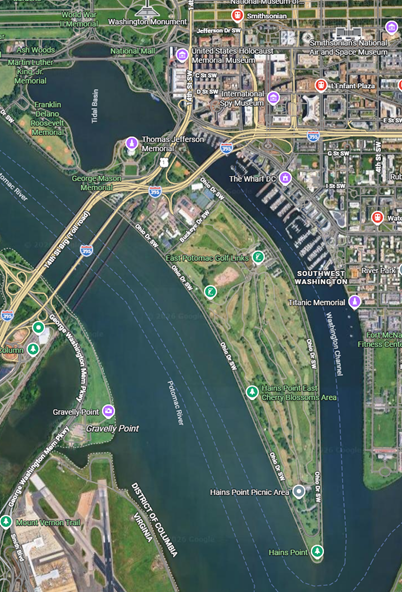 Aerial satellite view of a waterfront district showing parks, buildings, and industrial structures along a river.