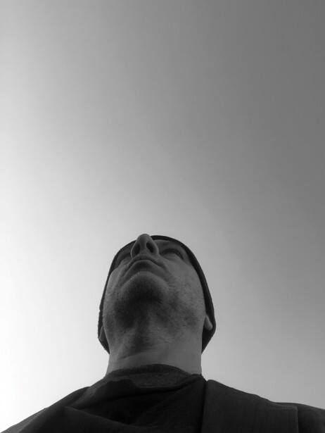 Black and white portrait of a person viewed from behind, shot against a plain gray background.