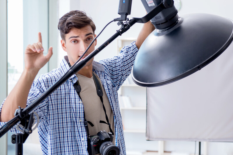 Photographer adjusting a large black reflector on a boom arm during a studio shoot.