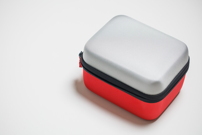 Red and white protective carrying case with gray cushioned lid and black zipper detail.