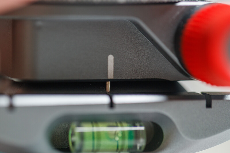 Close-up of a spirit level tool mounted on dark equipment with a red component visible on the right side.