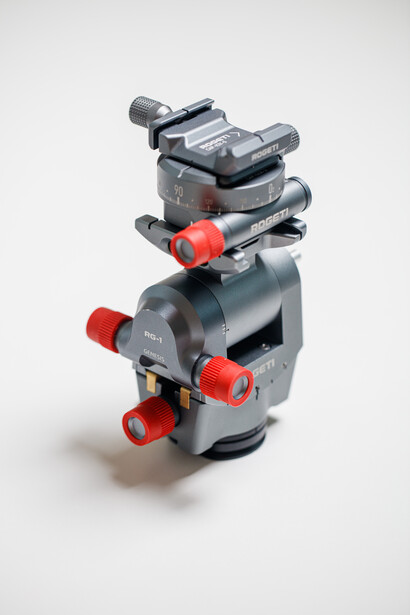 Stacked camera tripod heads with red leg locks and ball mounts against white background.