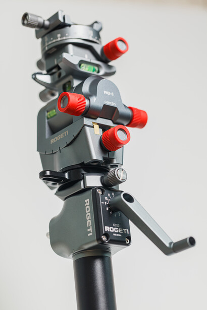 Professional camera tripod head with red knobs mounted on a black pole against white background.