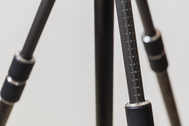 Close-up detail of tripod legs showing black rubber grips and metal bands against neutral background.