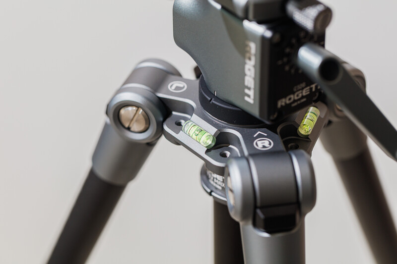 Close-up of a tripod head with spirit levels and pan-tilt controls mounted on aluminum legs.