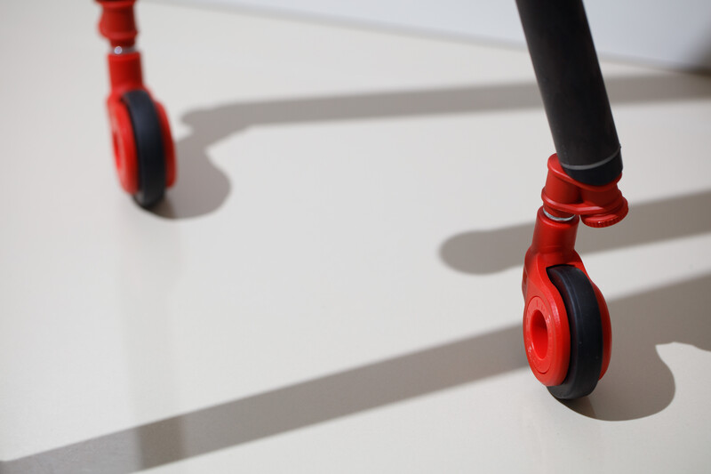 Red and black children's scooter with two wheels casting sharp shadows on white surface.