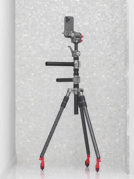 Professional camera gimbal with smartphone mount on tripod with red feet against textured white backdrop.