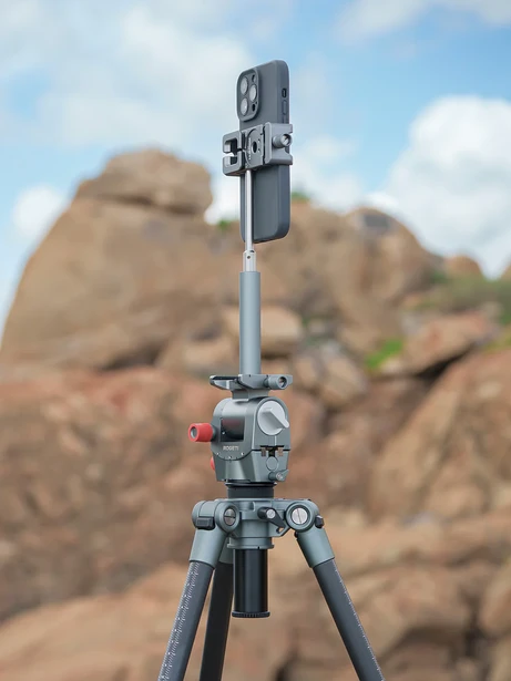 Smartphone mounted on a tripod with ball head against rocky hillside backdrop.