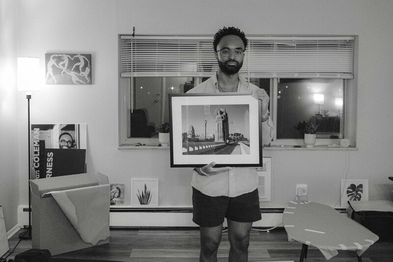 Photographer holding a framed black and white architectural photograph in a studio space.