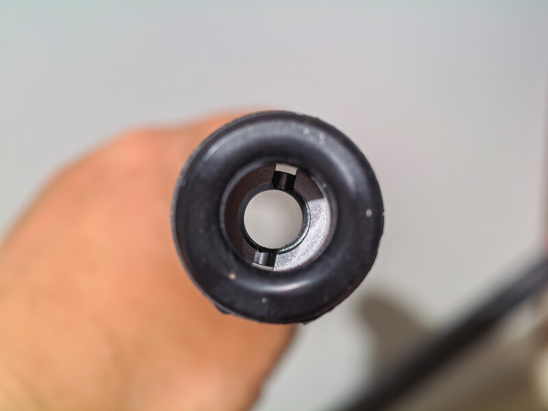 Close-up of a black camera lens cap viewed from the front, held in someone's hand against a blurred background.