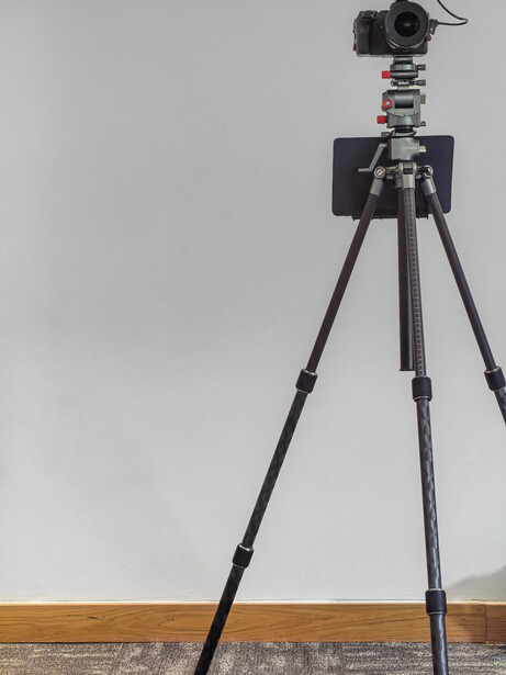 Professional camera mounted on tripod with ball head and vertical orientation bracket against neutral background.