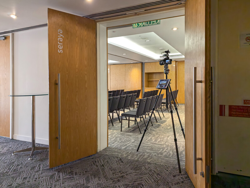 Professional video camera on tripod positioned in doorway of conference room with wooden doors and modern interior lighting.