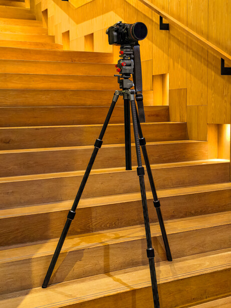 Professional camera mounted on tripod positioned on wooden staircase with warm lighting.