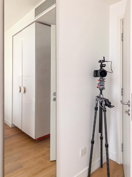 Camera mounted on tripod in minimalist white entryway with wooden flooring.