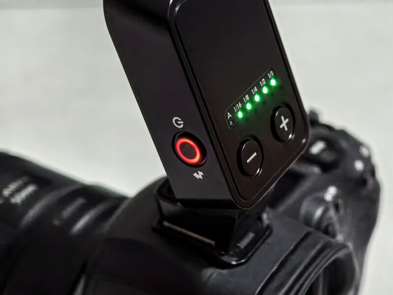 Close-up of a wireless flash trigger mounted on a camera hot shoe, showing control buttons and green status indicators.
