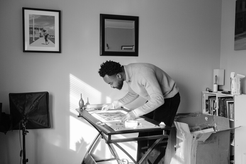 Photographer working at a standing desk in a bright studio space with natural light streaming across the work surface.