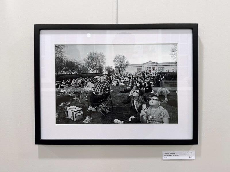 Framed black and white photograph of a large outdoor gathering with crowds of people and bare trees in the background.