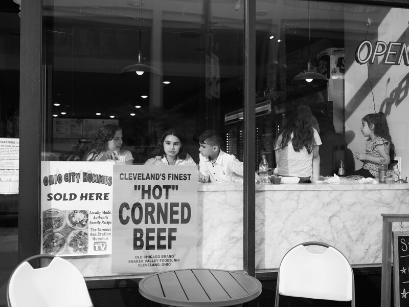 Black and white photograph of a deli counter window with signage advertising corned beef and customers visible inside.