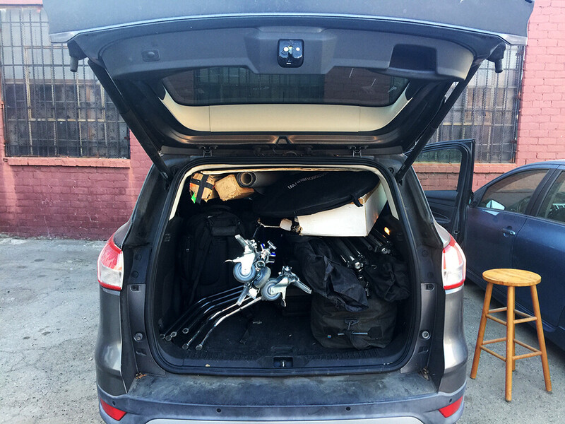 Open trunk of a dark sedan revealing a disassembled motorcycle inside against a brick building backdrop.