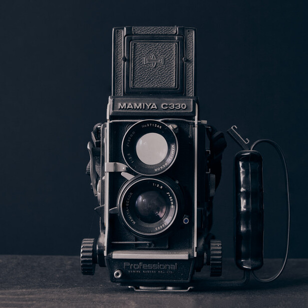 Mamiya C330 twin-lens reflex camera with professional accessories on dark background.