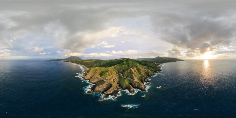 Aerial view of a lush green peninsula surrounded by deep blue ocean under dramatic cloudy skies.