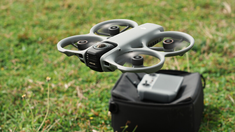 Compact quadcopter drone with four propellers positioned on grass beside its remote controller.