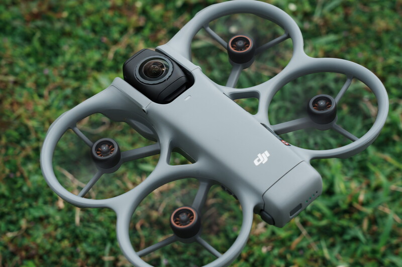 DJI Mini drone with gray propeller guards displayed overhead on grass background.