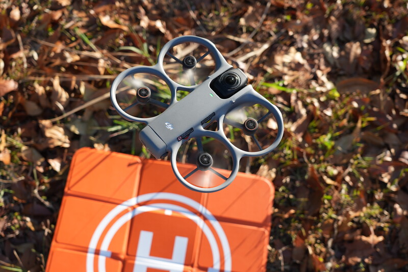 Compact quadcopter drone positioned above an orange calibration mat in an outdoor field setting.