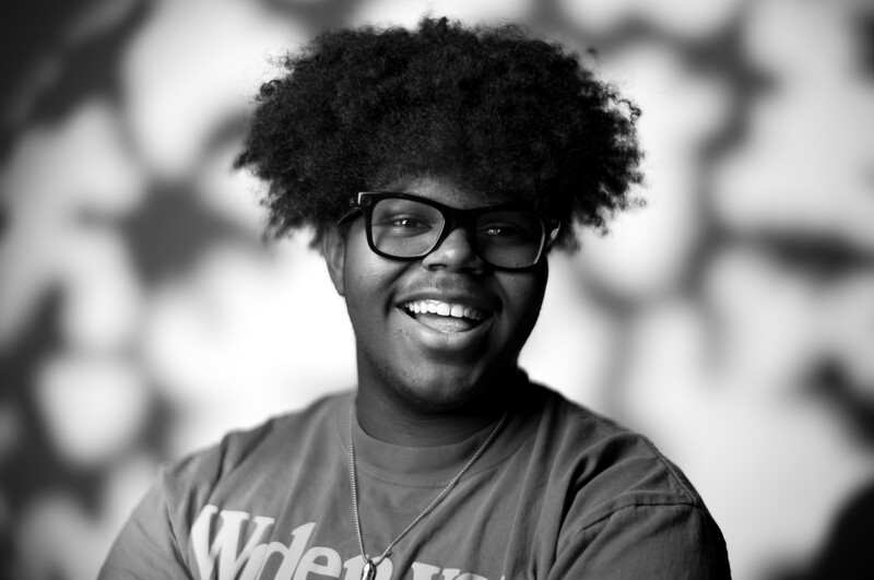 Smiling person wearing glasses and a t-shirt against a blurred bokeh background.