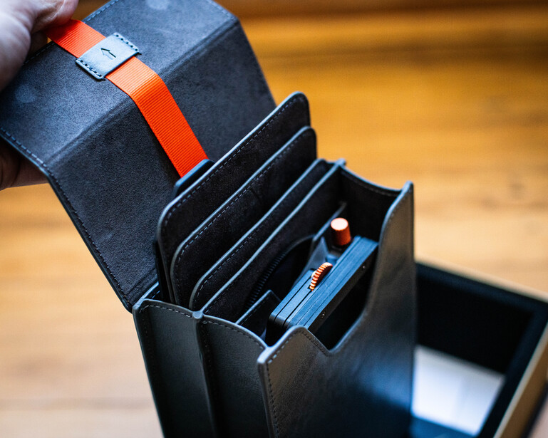 Black accordion wallet with red strap held open to display multiple card slots and compartments.