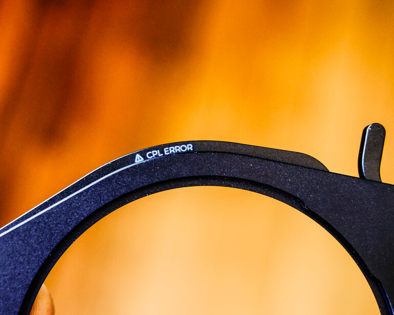 Close-up of a circular polarizing filter with text marking visible against warm orange and yellow bokeh background.
