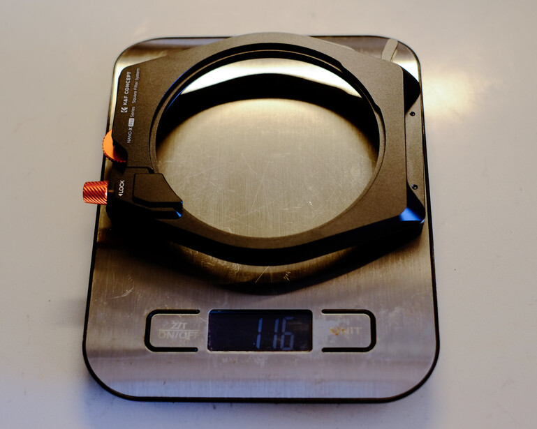 Circular camera filter mounted on a digital scale displaying 146 grams, with red and blue adjustment knobs visible on either side.