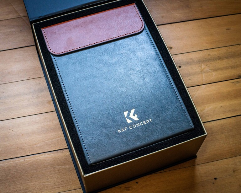Blue and pink leather wallet displayed in black presentation box on wooden floor.
