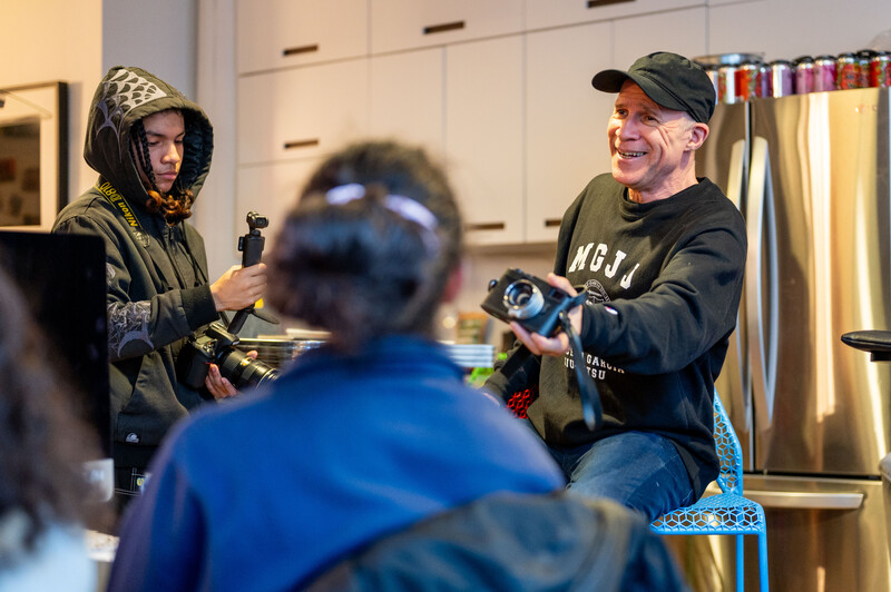 Two people demonstrating camera equipment during a workshop or training session with an audience member visible in foreground.