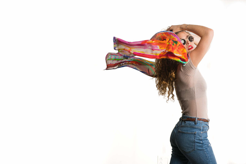 Woman holding a colorful patterned scarf above her head against a white background.