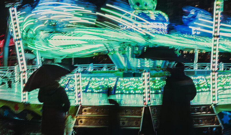 Silhouetted figures operating illuminated carnival ride controls at night.