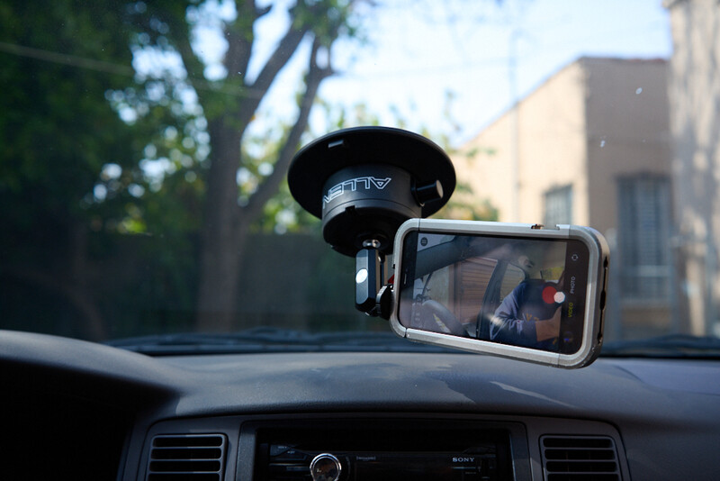 Smartphone mounted on car dashboard with suction cup holder, displaying video footage during daytime.