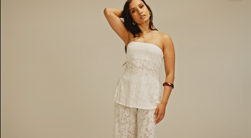 Woman in strapless white lace top and matching pants standing against neutral background.