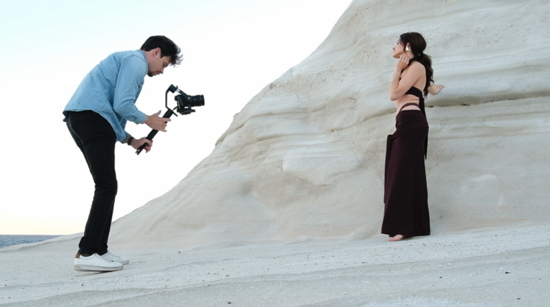 Cameraman operating a gimbal stabilizer while filming a woman posing against a white textured cliff face.