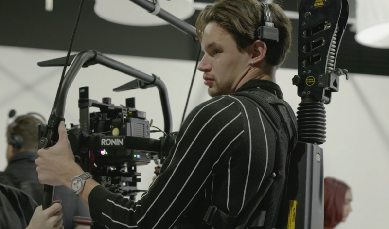 Cinematographer operating a cinema camera rig with professional microphone and support equipment.