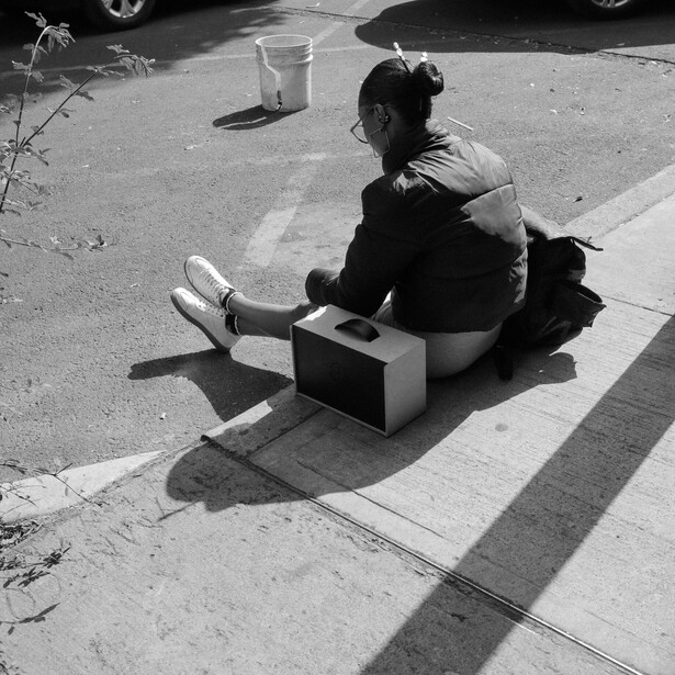 Person sitting on pavement with vintage boombox, shot from above in black and white.