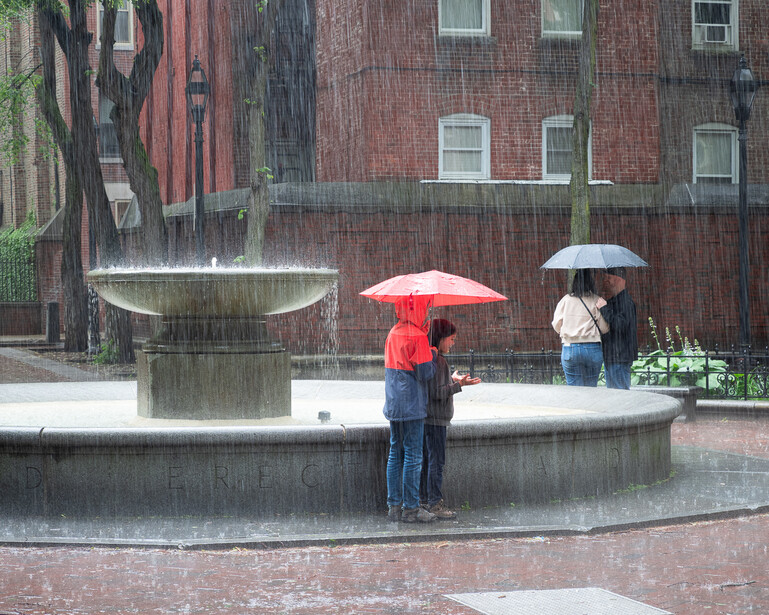 Street photograph of people hiding from rain under umbrellas