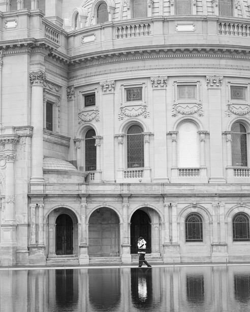 Black and white street photo of guard walking by building