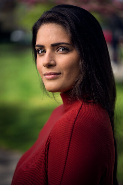 Woman in red textured garment looking over shoulder with natural outdoor lighting.